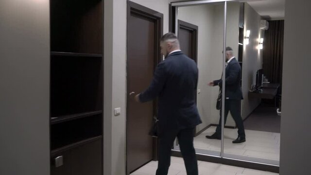 Mature businessman leaves a hotel room turning off the light and opens the door.