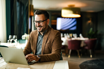 Happy man using laptop at restaurant, portrait.