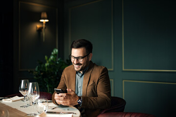 Handsome smiling man using smart phone at restaurant, portrait, copy space.