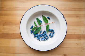 honeysuckle berries, green leaves in a white plate on a background of wood