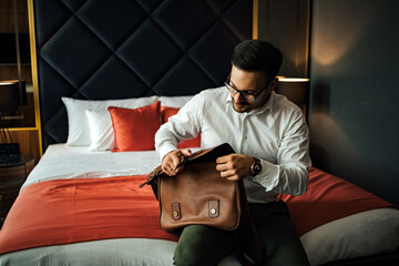 Elegant businessman sitting on the edge of the bed in the hotel room, portrait.