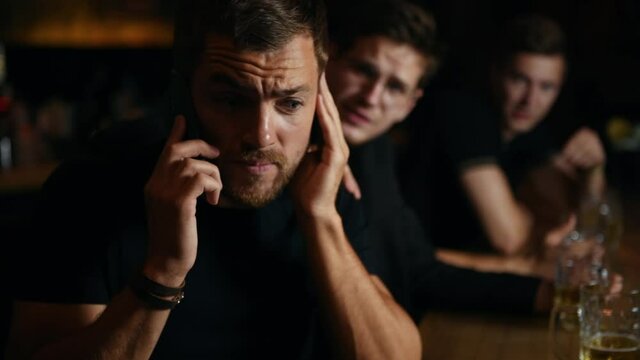 Man talks by the phone, friends won't let him go. Three sports fans in a bar watching soccer. With beer.