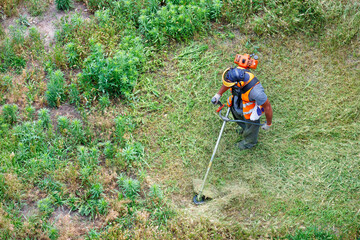 Worker mows tall grass with an industrial petrol trimmer, top view.