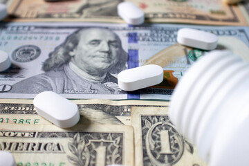 White pills and a medical bottle on one and one hundred dollar bills. Health insurance concept. Medicine and money. Medical background.