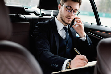 Businessman writing in notebook sitting in luxury car