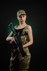a sexy girl in military airsoft overalls poses with a assault rifle on a dark background