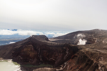 Daytime view of the mouth of an active volcano. Clouds on the horizon, mountains, volcanic lake are visible.