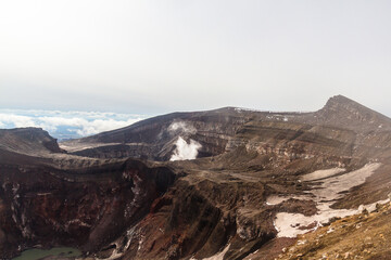 Daytime view of the mouth of an active volcano. Clouds on the horizon, mountains, volcanic lake are visible.