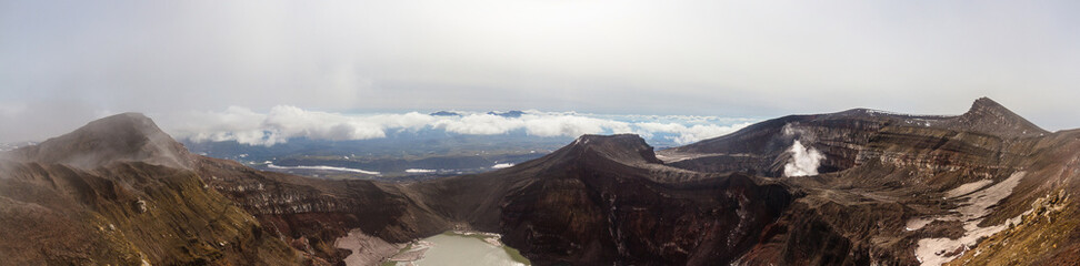 Daytime view of the mouth of an active volcano. Clouds on the horizon, mountains, volcanic lake are visible.