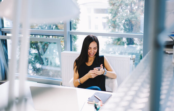 Cheerful attractive editor satisfied with occupation messaging via mobile phone, business woman in elegant wear happy to receive good advertising offer on email box while sitting in office indoors - Powered by Adobe