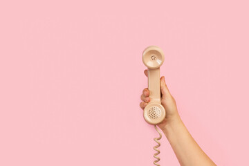Mano de mujer sosteniendo el tubo retro de un teléfono antiguo sobre fondo rosa liso y aislado....
