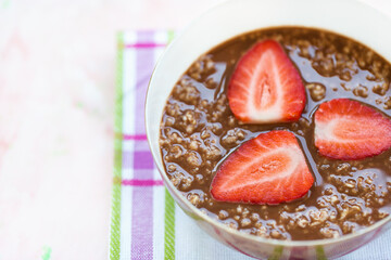 Chocolate oatmeal porridge and strawberries, summer breakfast in bowl on pink background, concept of healthy eating vegan food. Close up, selective focus, copy space