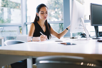 Concentrated professional female journalist making researches on website analyzing and noting...