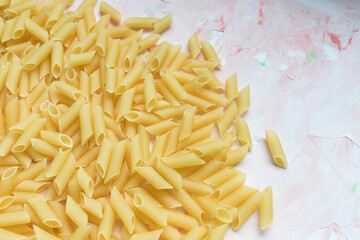 Raw traditional Italian penne pasta on pink background. Close up, copy space