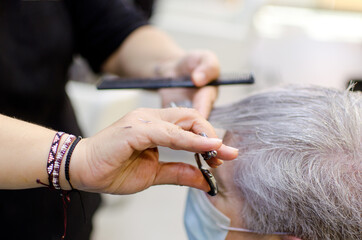 Mano de peluquera cortando el pelo a mujer de pelo blanco con mascarilla