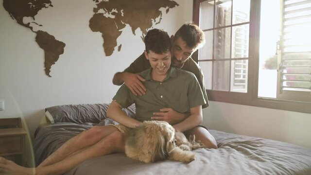 Gay boy couple lying in bed with their dog. LGBT
