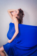 Sexy and Fit 8 Months Pregnant Woman Covered in Blue Tulle, from Profile, on Grey Background....