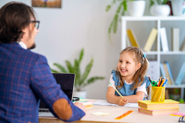 ?ute little girl is engaged in lessons with a teacher at home.