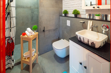 Modern loft interior of bathroom. White sink and toilet. Brick wall. Grey tile. Red door.