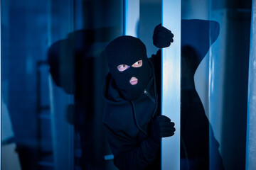 Burglar peeking into the house through an open glass door