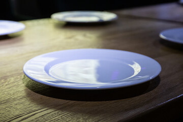 Table setting in the restaurant is ready and waiting for guests
White plate on a wooden table in a restaurant in the background, blurred three more plates out of focus