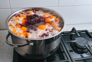 Fresh fruits are boiled in boiling water in a metal pan on the stove. Delicious stewed apricot, apples, cherries, raspberries. Photography, concept.