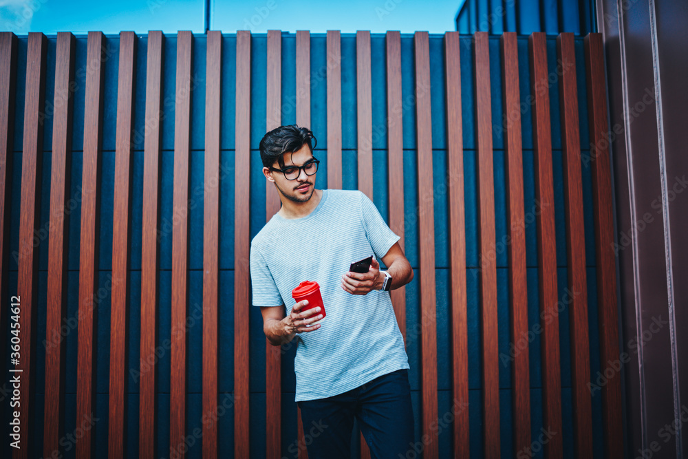 Poster stylish male blogger checking mail in networks on smartphone connected to 4g internet standing with 