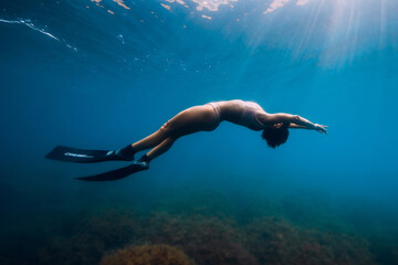 Sporty woman freediver with fins glides underwater in blue sea.