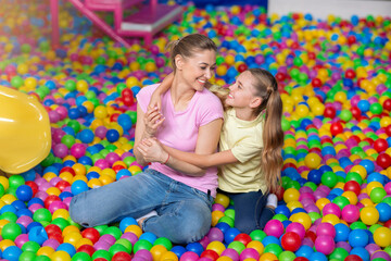 Smiling mom with her daughter hugging in ball pond at indoor amusement park
