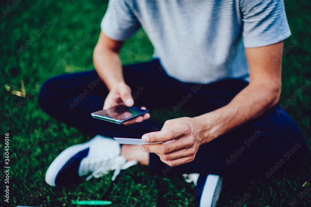 Poster cropped image of young man dialing number on smartphone using information from visit card, hipster g