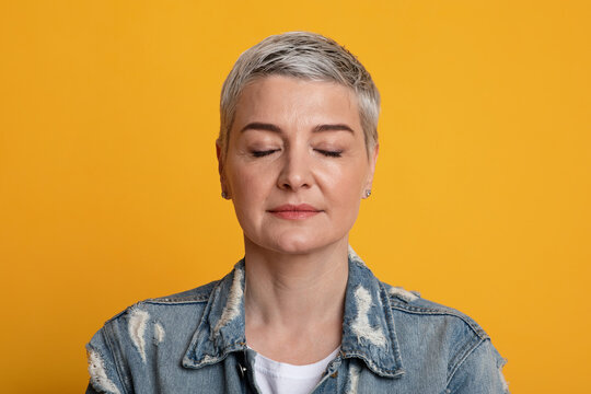 Portrait Of Calm Beautiful Mature Womanstanding With Closed Eyes Over Yellow Background