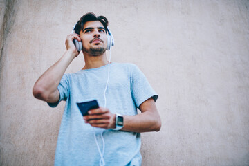 Cheerful hipster guy in modern headphone listening new song from internet radio website using...