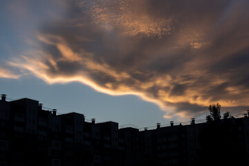 Stratocumulus clouds illuminated by the setting sun against a blue sky, clouds above the city block. Nature background.