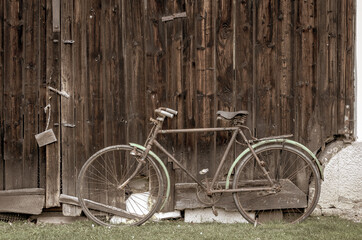 Fototapeta na wymiar Old vintage bike on green grass leaning against the old wooden barn door, photo with retro vintage filter effect