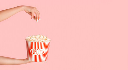 Cropped view of young girl holding jumbo bucket of popcorn on pink background, free space © Prostock-studio