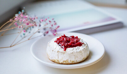 Camembert cheese baked with berry sauce on the background of the magazine. Light daylight