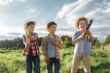 Excited boys popping cracker.. Playful little boys in t-shirt and hat exploding party popper standing on field