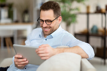 Happy man using digital tablet sitting on sofa - Powered by Adobe