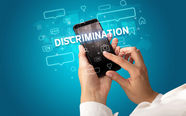 Female hand typing on smartphone with DISCRIMINATION inscription, social media concept