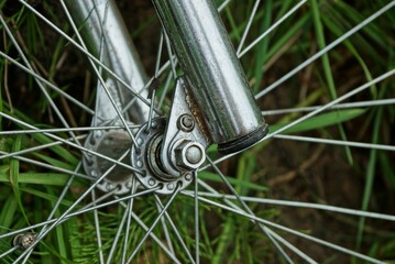 part of a bicycle with a gray iron  fork and spokes on a wheel against a background of green grass