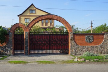 iron red gate with forged black pattern and stone wall of the fence on the street