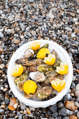Big white plate with fresh delicious oysters and lemon. Light lunch on the beach,  north of France, Normandie. Atlantic ocean coast. Close up. Top view flat lay