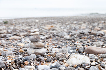 Grey pebble stones pyramid on the beach. Concept of zen, stability, harmony, balance. Close up, macro. front view. Blue ocean water on the background. North of France, Normandy.