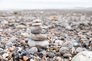 Grey pebble stones pyramid on the beach. Concept of zen, stability, harmony, balance. Close up, macro. front view. Blue ocean water on the background. North of France, Normandy.