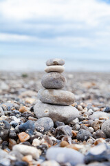 Grey pebble stones pyramid on the beach. Concept of zen, stability, harmony, balance. Close up, macro. front view. Blue ocean water on the background. North of France, Normandy