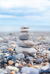 Fototapeta na wymiar Grey pebble stones pyramid on the beach. Concept of zen, stability, harmony, balance. Close up, macro. front view. Blue ocean water on the background. North of France, Normandy