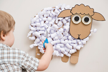 The boy cuts a paper sheep. DIY toy. Activity at home. Early education, fine motor skills. Montessori methodology.
