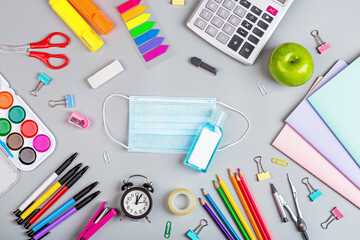 school supplies with medical face mask on a gray background. Protection of schoolchildren and students from the coronavirus covid-19, schooling in a pandemic. Flat lay, top view, mockup, template