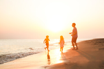 Fototapeta premium happy family father and two children playing on the beach run at the sunset time. 