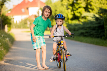 Obraz premium Older brother, helping his little brother to learn how to ride a bike, holding him and teaching him